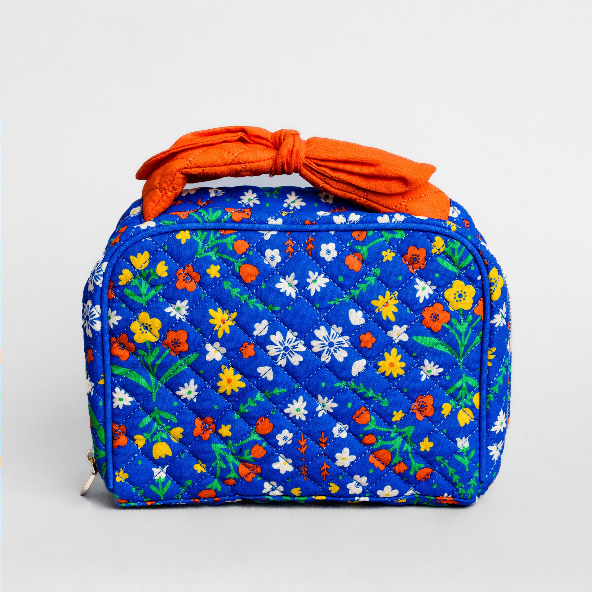 A quilted cosmetic bag with a vibrant blue background and a colorful floral print, featuring a prominent orange fabric top handle, shown on a light gray background.