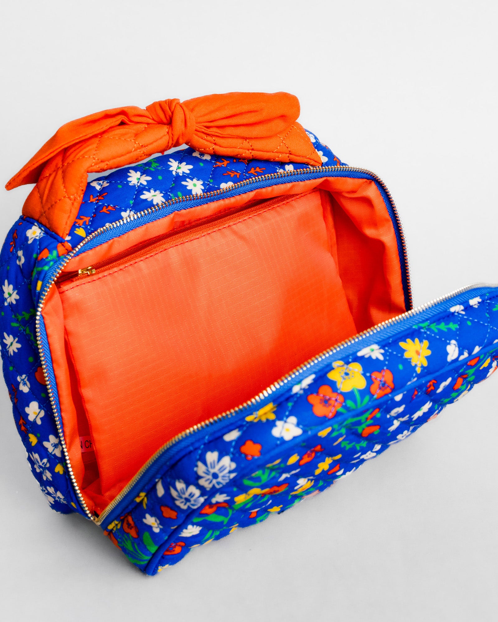 A blue floral zippered pouch with a bright orange interior and a matching orange fabric bow on top, shown open on a light gray background.