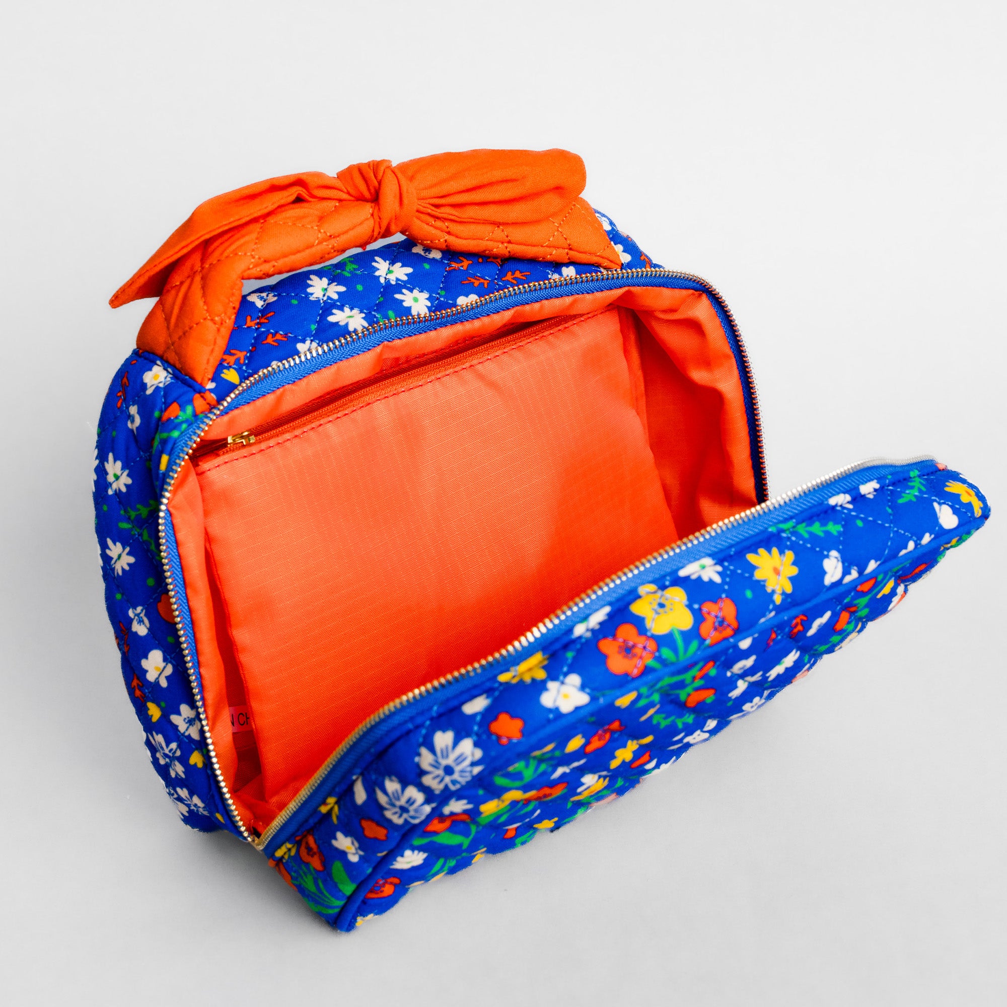 A blue floral zippered pouch with a bright orange interior and a matching orange fabric bow on top, shown open on a light gray background.