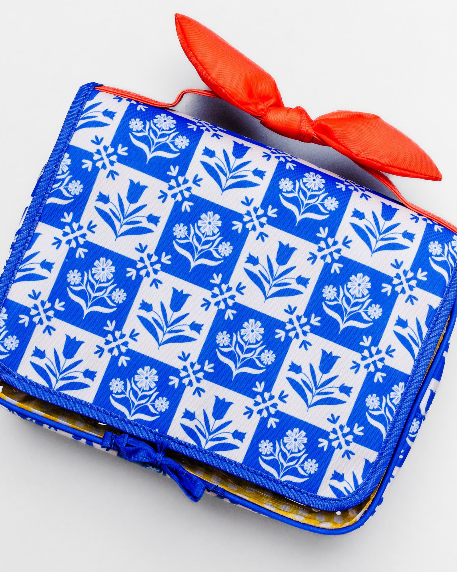 A blue and white patterned clutch bag with a bright red bow on top, photographed on a clean white background.