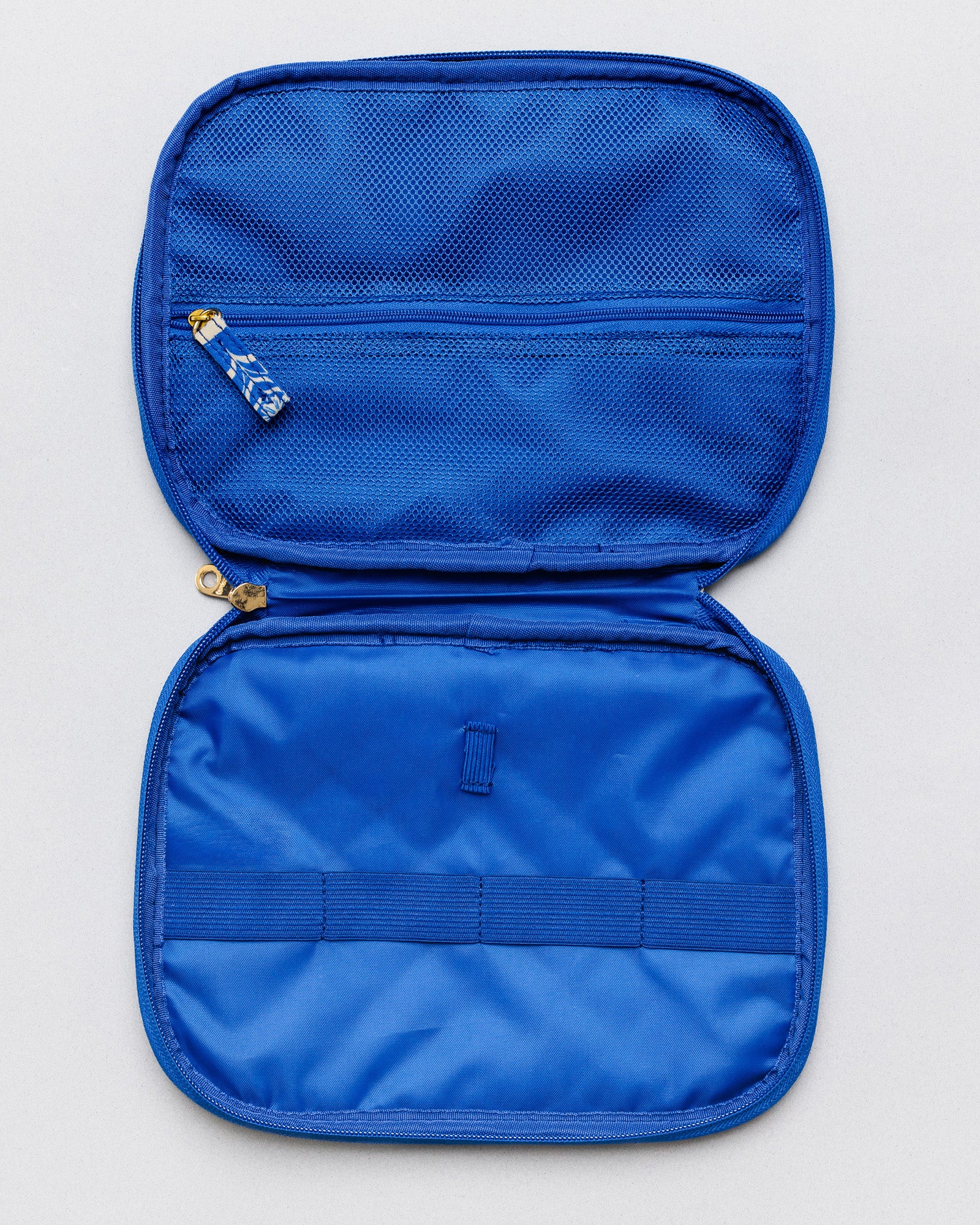 A bright blue zippered travel organizer case shown open against a light gray background, featuring two compartments, a zip pocket with a blue-and-white patterned zipper pull, and an elastic band across the lower section.
