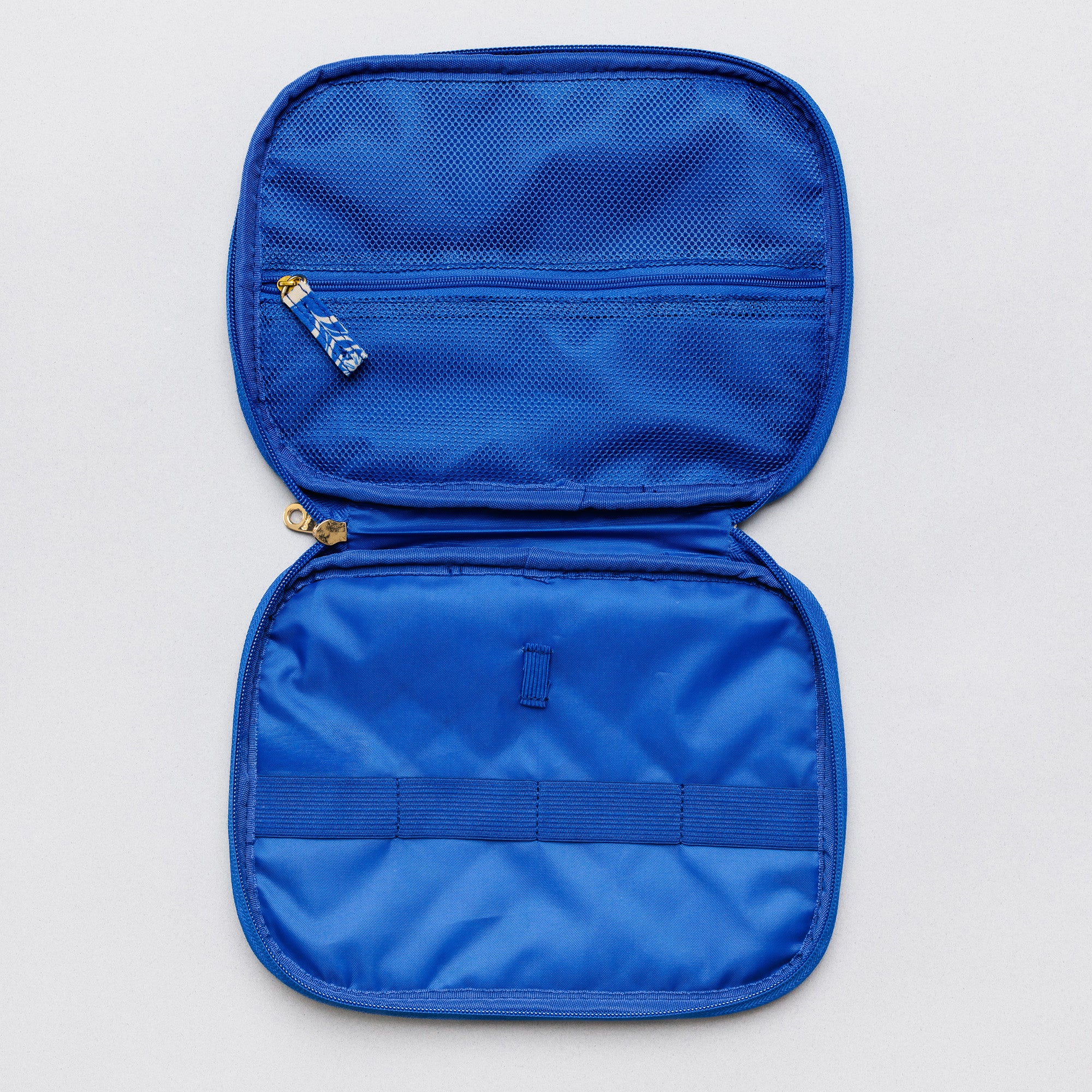 A bright blue zippered travel organizer case shown open against a light gray background, featuring two compartments, a zip pocket with a blue-and-white patterned zipper pull, and an elastic band across the lower section.
