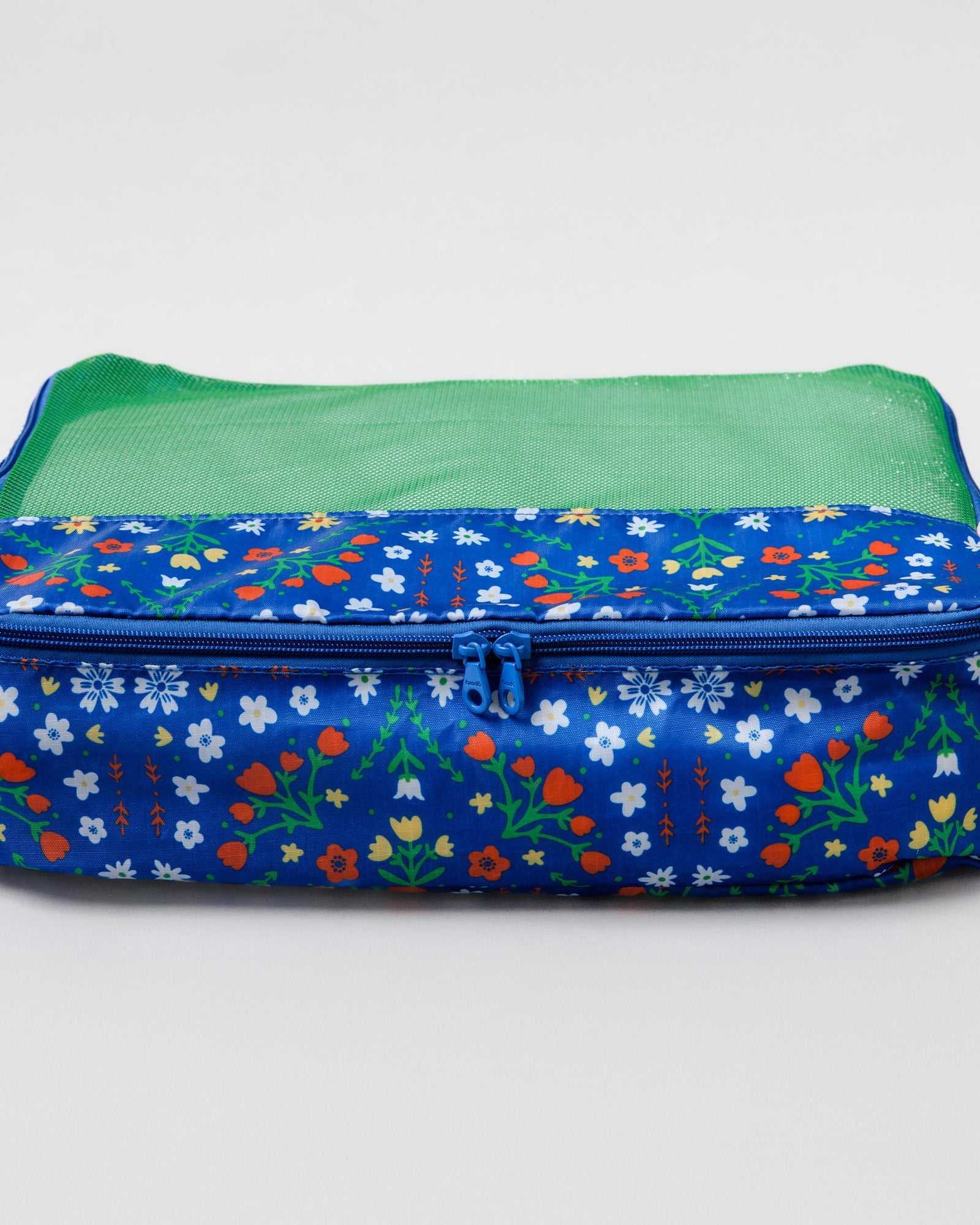 A rectangular zippered travel organizer bag with a blue floral print exterior and a green mesh interior, shown on a light gray background.