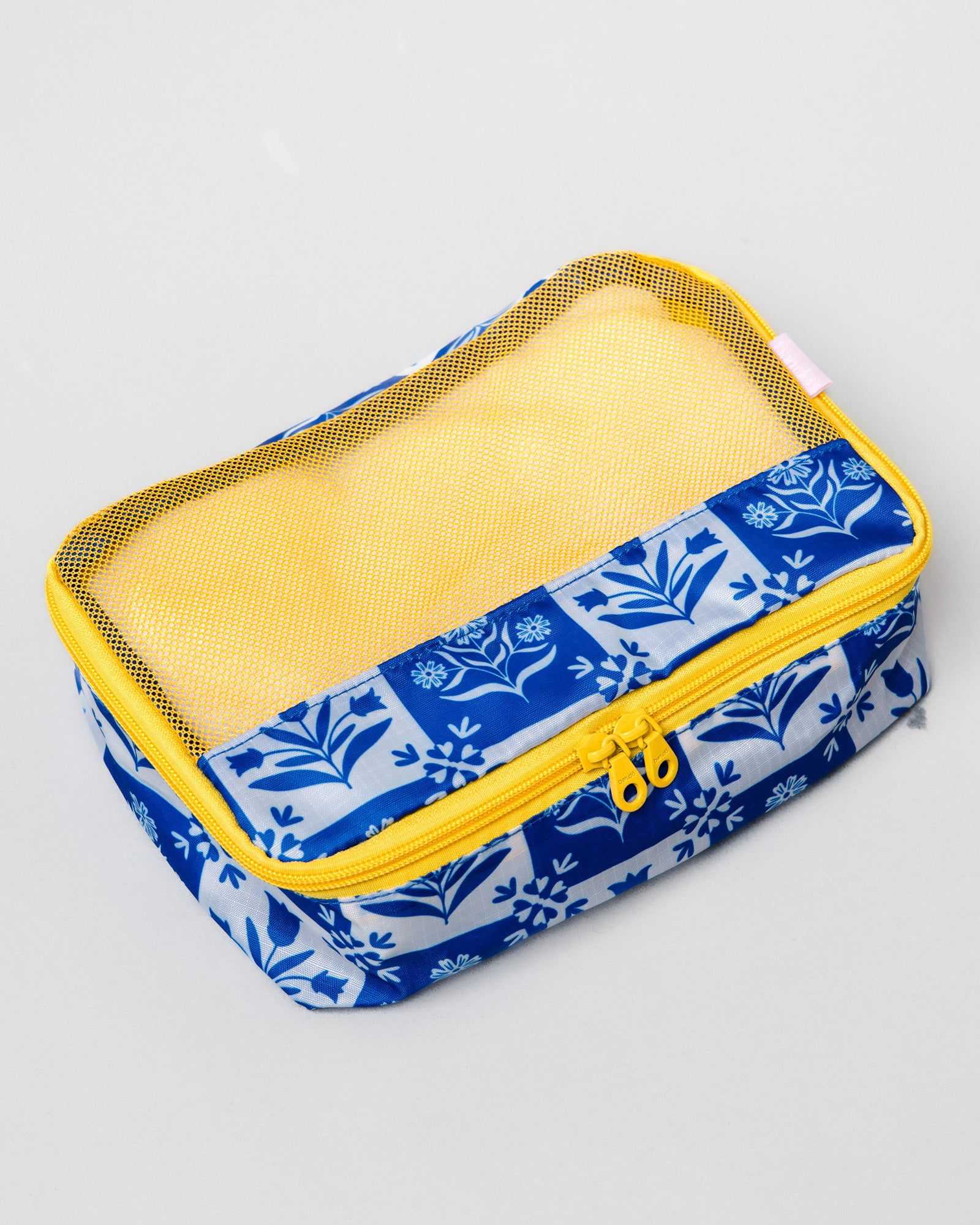 A rectangular fabric pouch with a blue and white floral patterned exterior, a yellow mesh window, and a yellow zipper, shown on a light gray background.