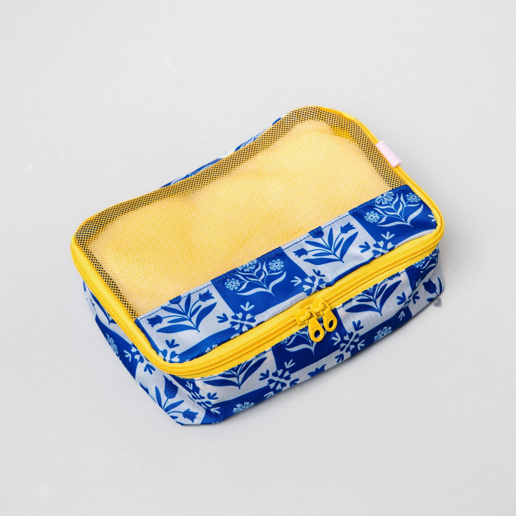 A rectangular fabric pouch with a blue and white floral patterned exterior, a yellow mesh window, and a yellow zipper, shown on a light gray background.