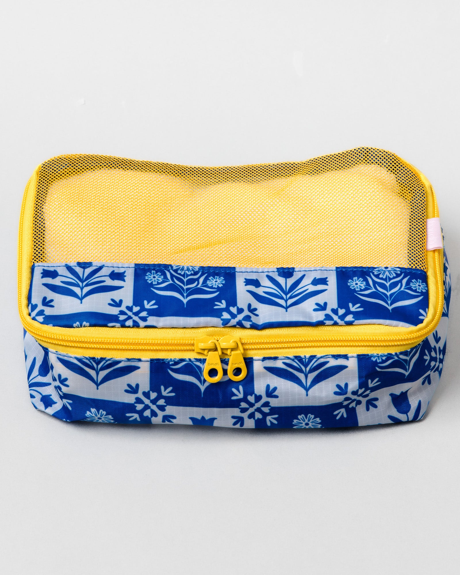 A rectangular mesh organizer pouch with a blue and white floral patterned fabric base, a yellow zipper, and a yellow mesh top, shown on a light gray background.