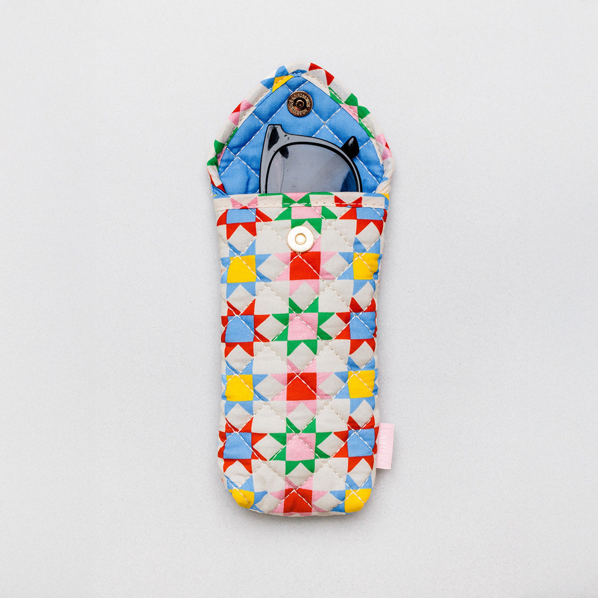 A quilted fabric pouch with a colorful geometric star pattern in red, yellow, green, blue, and pink on a white background, shown with a pair of sunglasses inside on a light gray background.