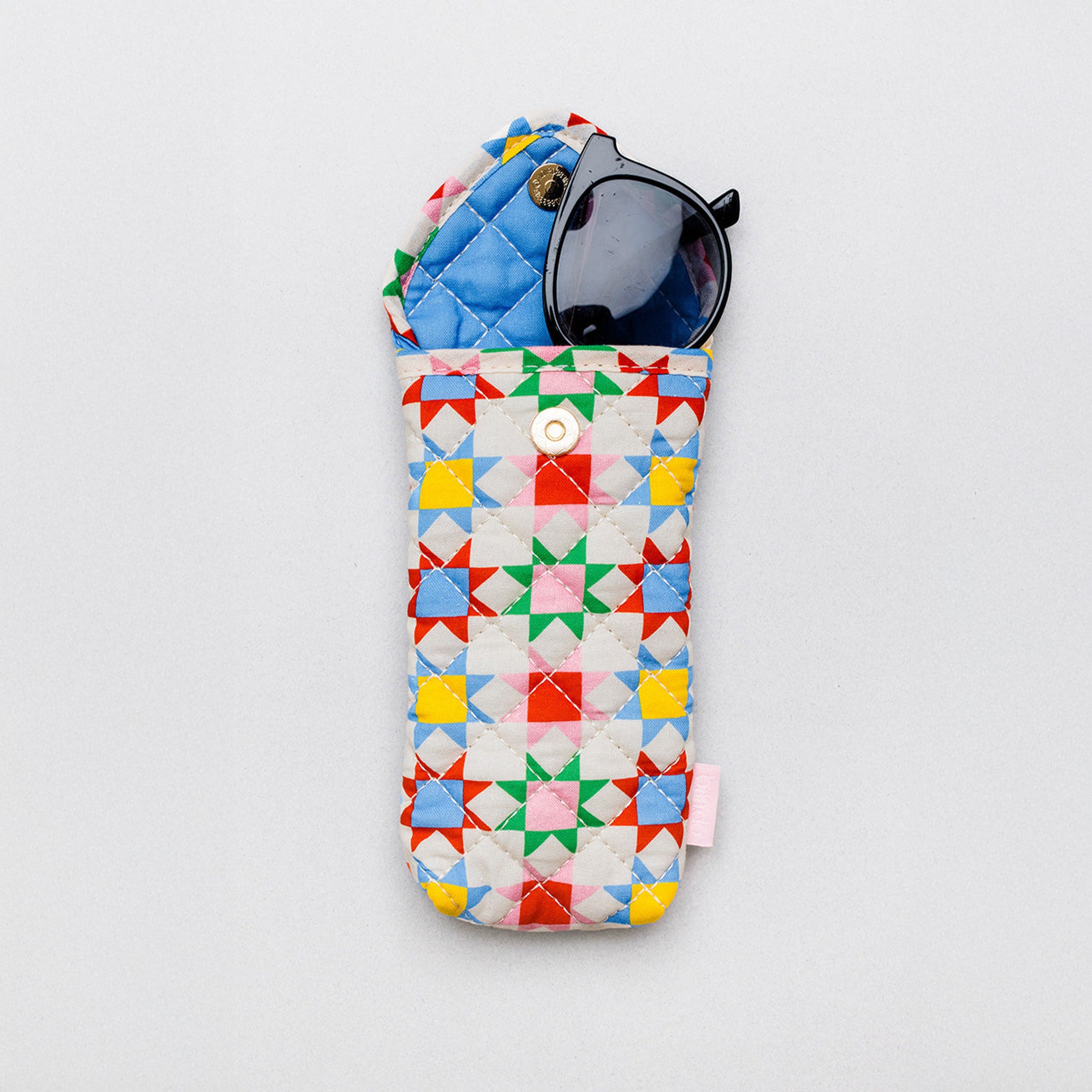 A quilted fabric sunglasses case with a colorful geometric star pattern, shown on a light gray background with black sunglasses inside.