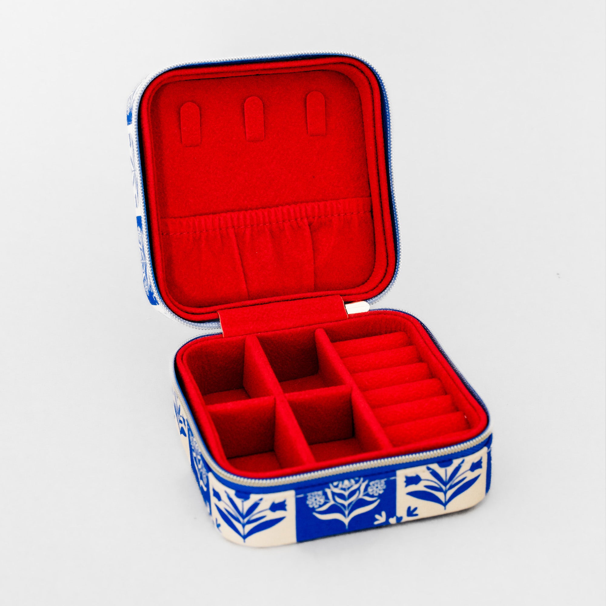 An open fabric jewelry box with a red velvet interior and a blue and white floral patterned exterior, shown on a light gray background.