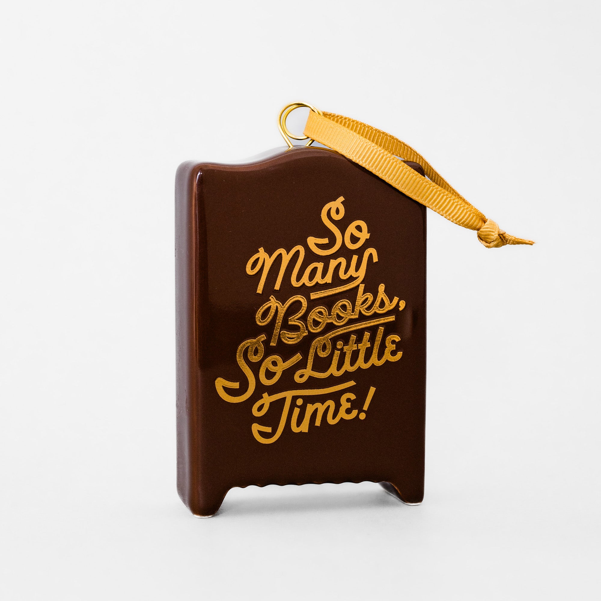 A brown book-shaped ornament with gold lettering that reads 'So Many Books, So Little Time!' and a gold ribbon hanger, shown on a clean white background.