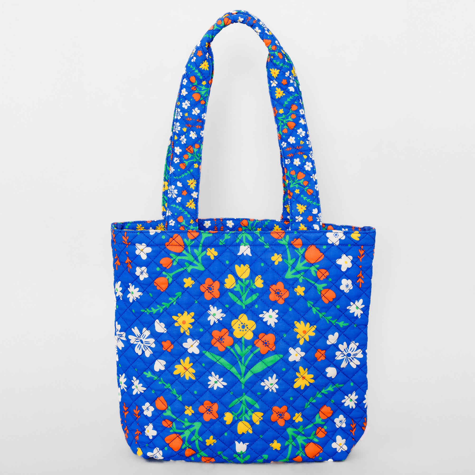 A quilted blue tote bag with a colorful floral pattern, featuring green stems and leaves, orange and yellow flowers, and small white blossoms, set against a plain light gray background.