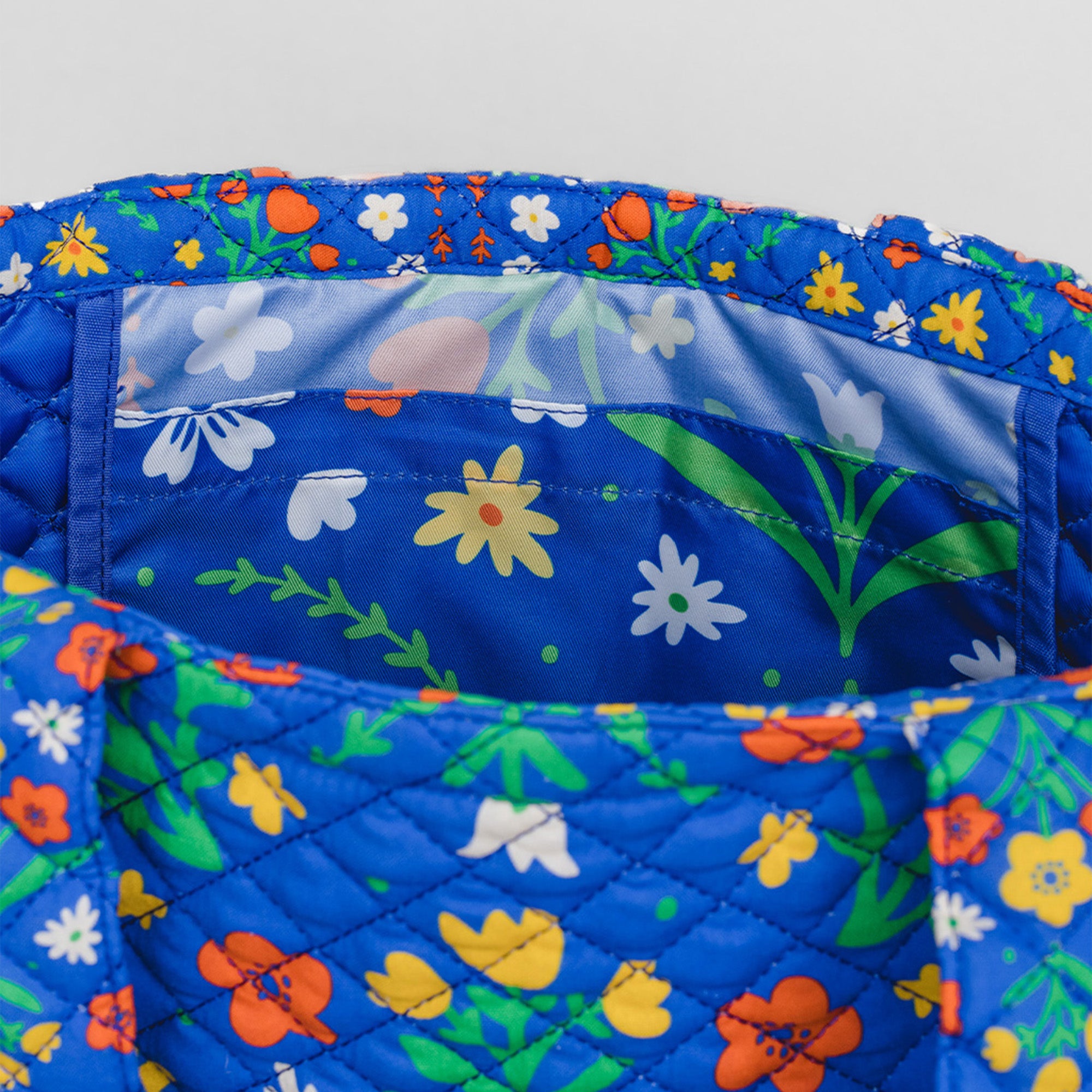 Close-up of a quilted fabric bag or pouch with a bright blue background and a multicolor floral print, showing the interior lining with white tulips and green stems.
