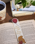 Open book with a bookmark featuring a bear holding a balloon, next to a mug with a bear design on a wooden surface.