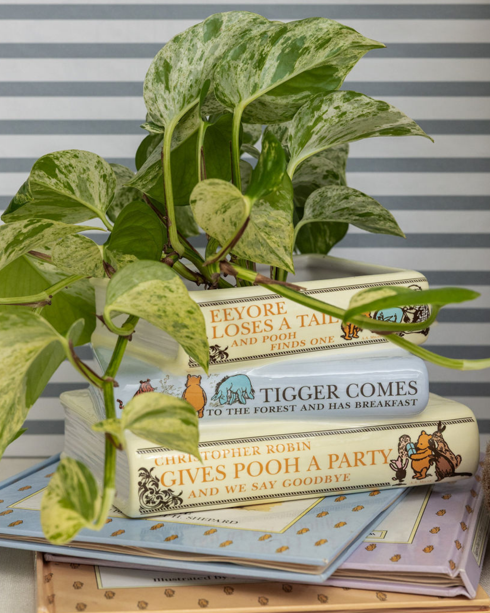 Stack of children's books with a plant and teddy bear on a striped background