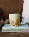 Mug with Winnie the Pooh design on a stack of books with a teddy bear in the background