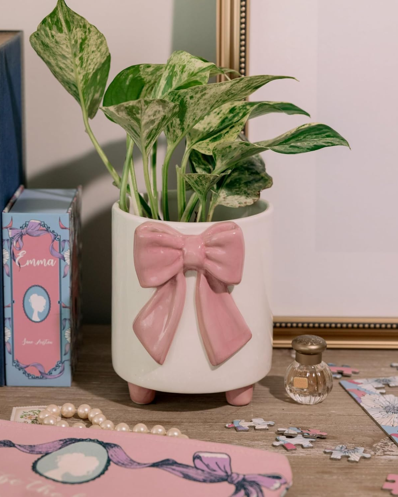 Decorative plant pot with a pink bow on a table with books and a puzzle.