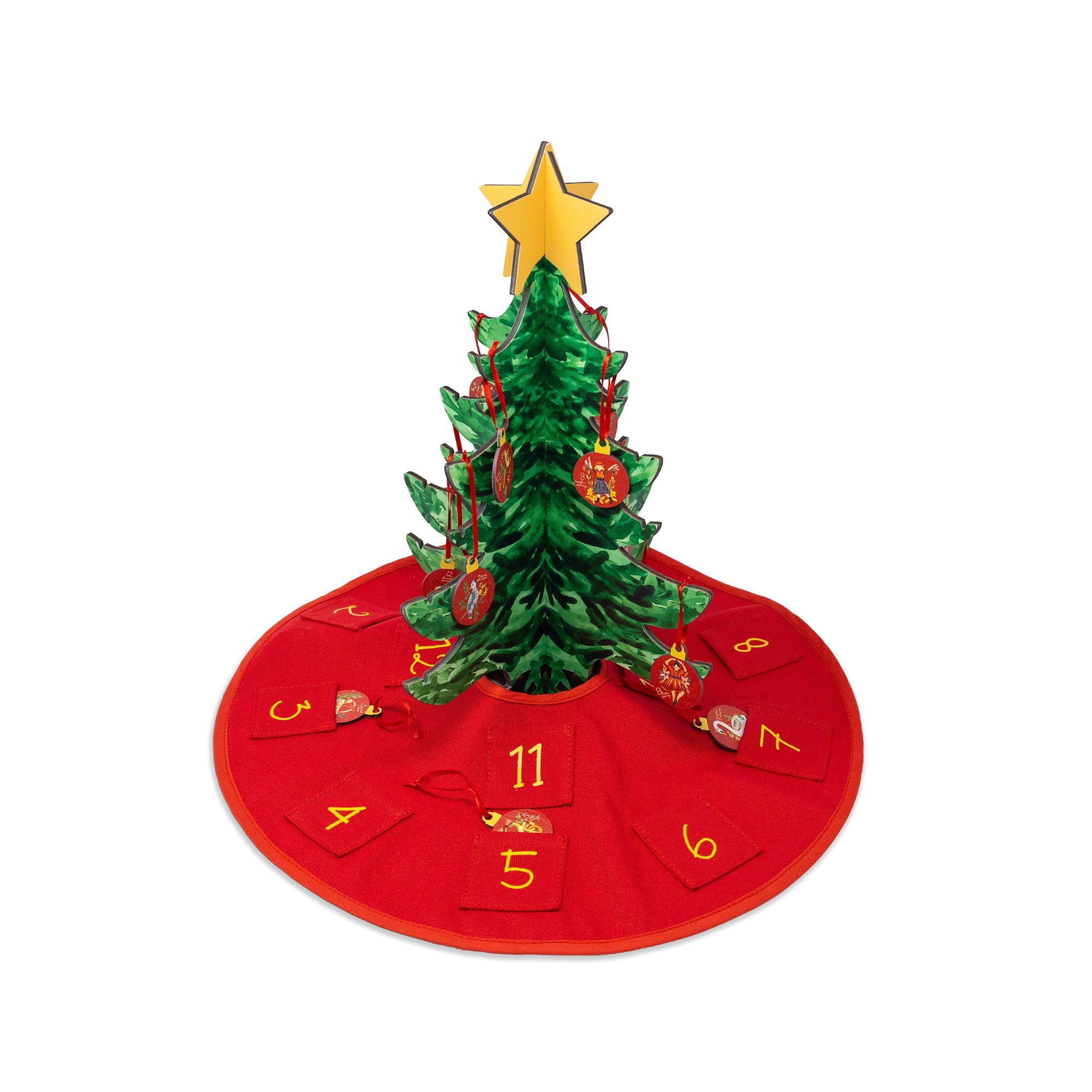A green Christmas tree with a gold star topper, decorated with red ornaments, standing on a red circular advent skirt with numbered pockets around it, isolated on a white background.