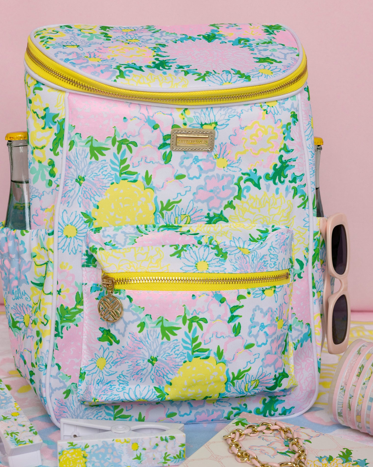 Floral-patterned cooler bag with sunglasses and a bottle on a pink background