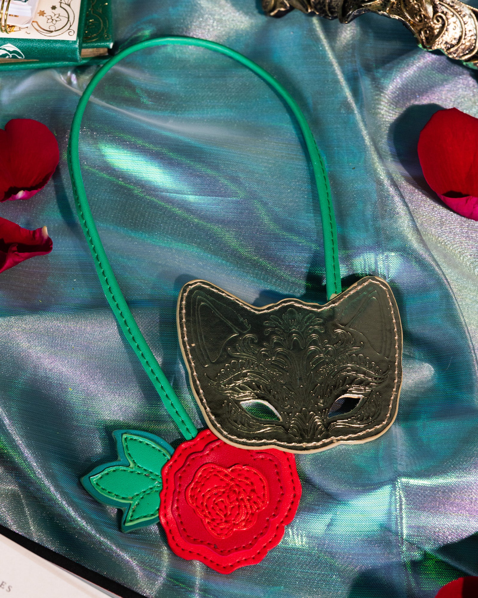 Gold mask with green strap and red rose bookmark on a silky teal cloth