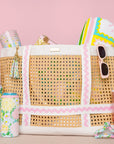Woven tote bag with colorful accessories on a pink background