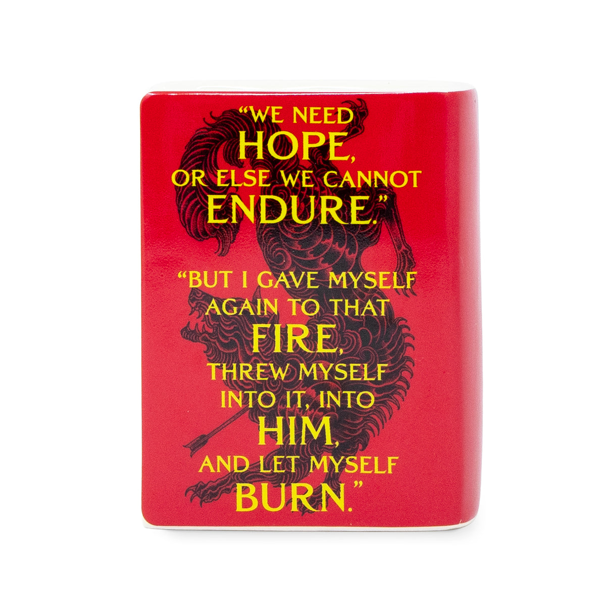 A red ceramic candle featuring a black creature illustration and two quotes in yellow text, shown on a plain white background.