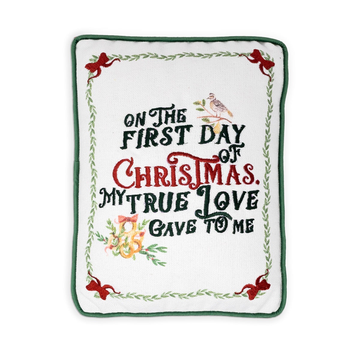 A square white embroidered pillow or cushion with a green border and festive text reading 'On the first day of Christmas, my true love gave to me,' decorated with red bows, green leaves, and small holiday illustrations.