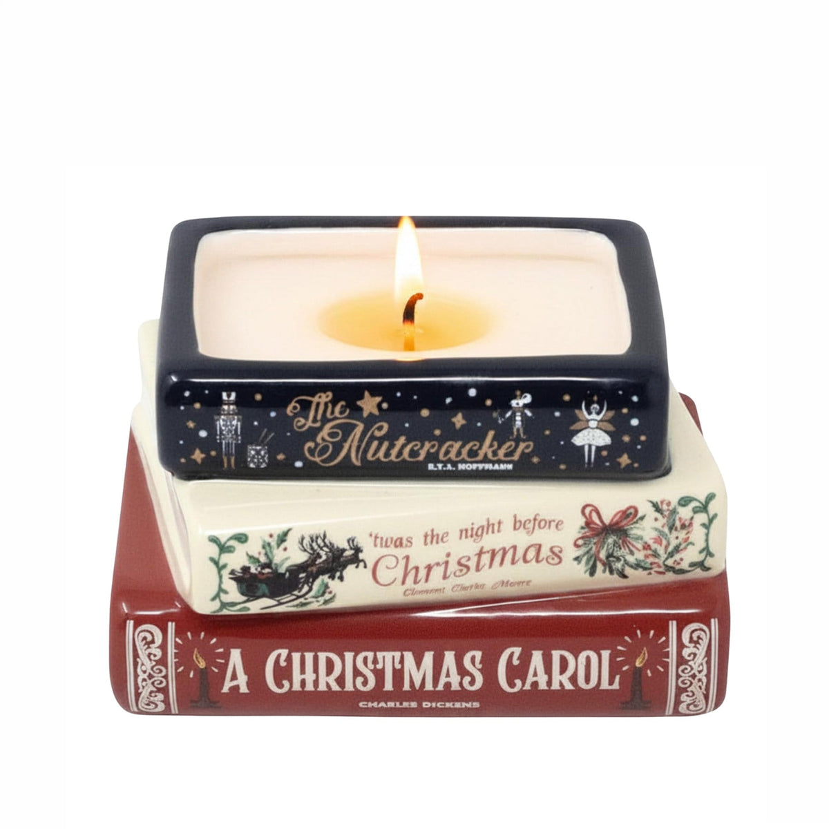 A square ceramic candle holder styled like a stack of Christmas books, with a lit candle inside. The top book is dark navy blue with gold Nutcracker illustrations and text; the middle book is cream with red and green holiday text and illustrations; the bottom book is dark red with white text reading 'A Christmas Carol.'