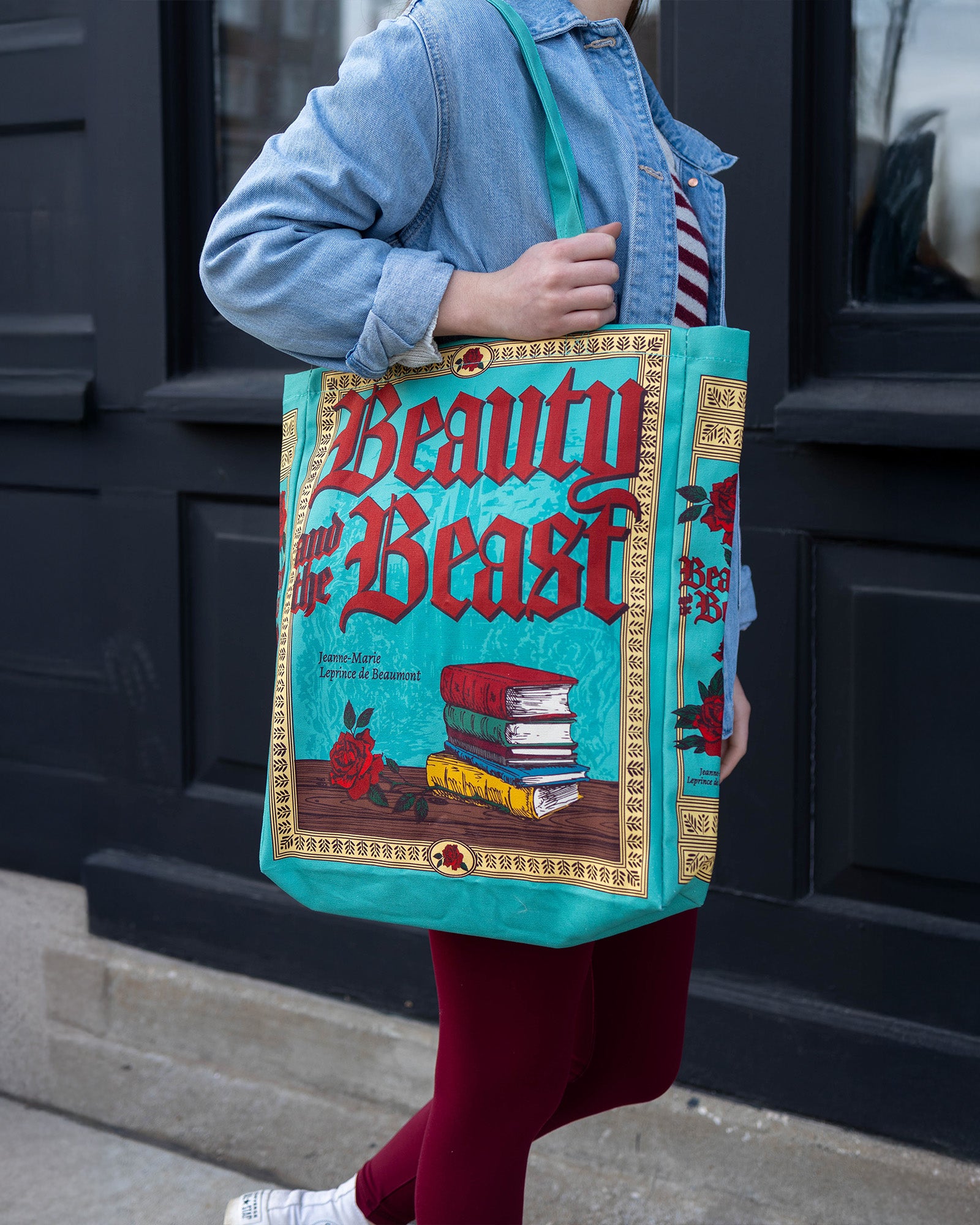 Person holding a 'Beauty and the Beast' themed tote bag in front of a dark door.