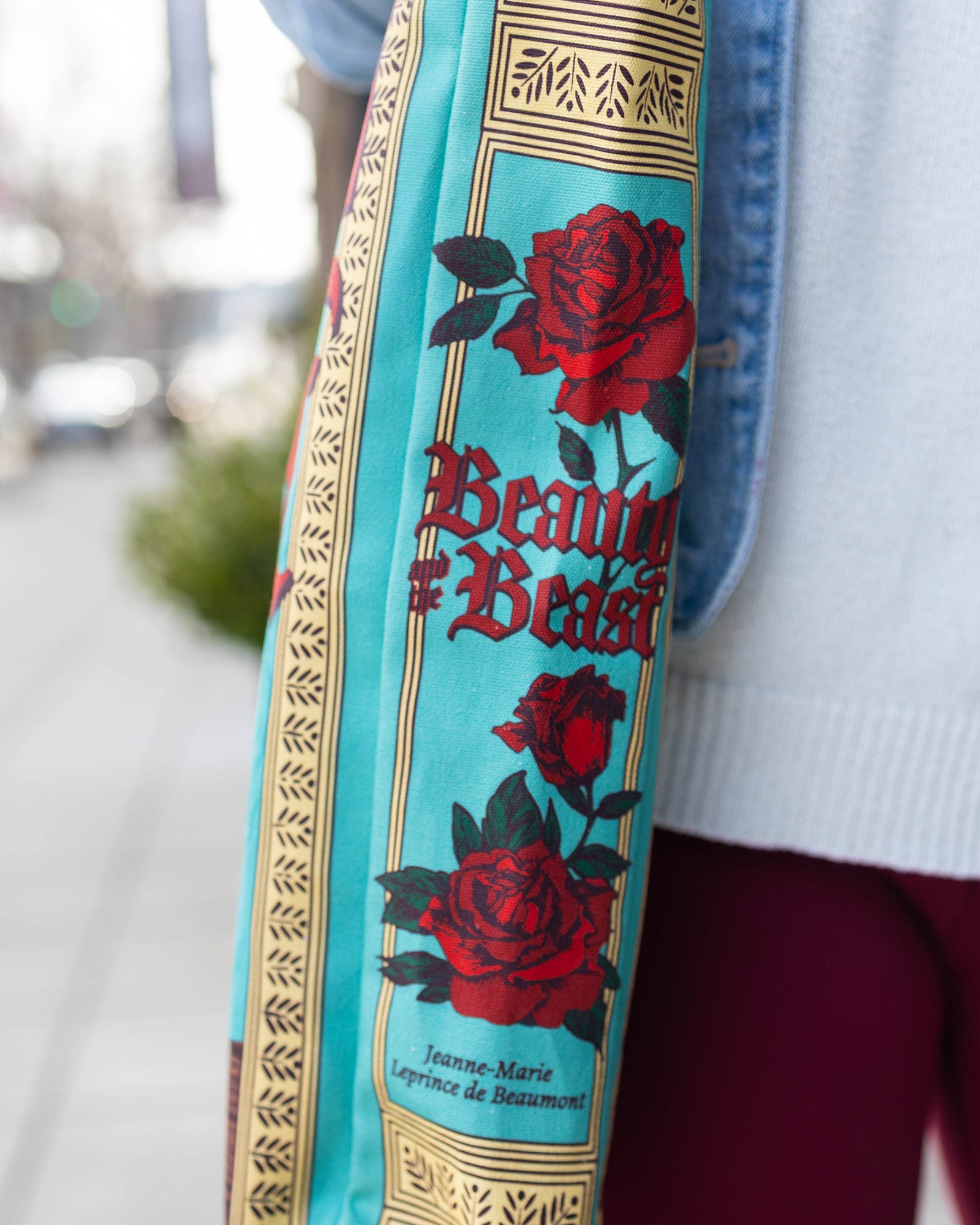 Close-up of a bag strap with 'Beauty and the Beast' design featuring roses and text.