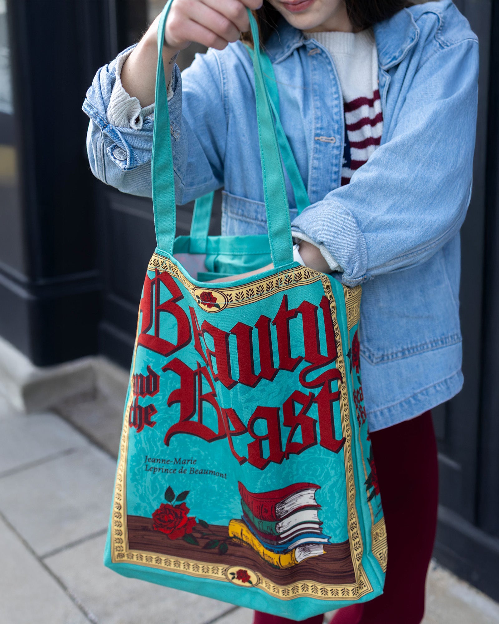 Person holding a 'Beauty and the Beast' book-themed bag on a sidewalk.