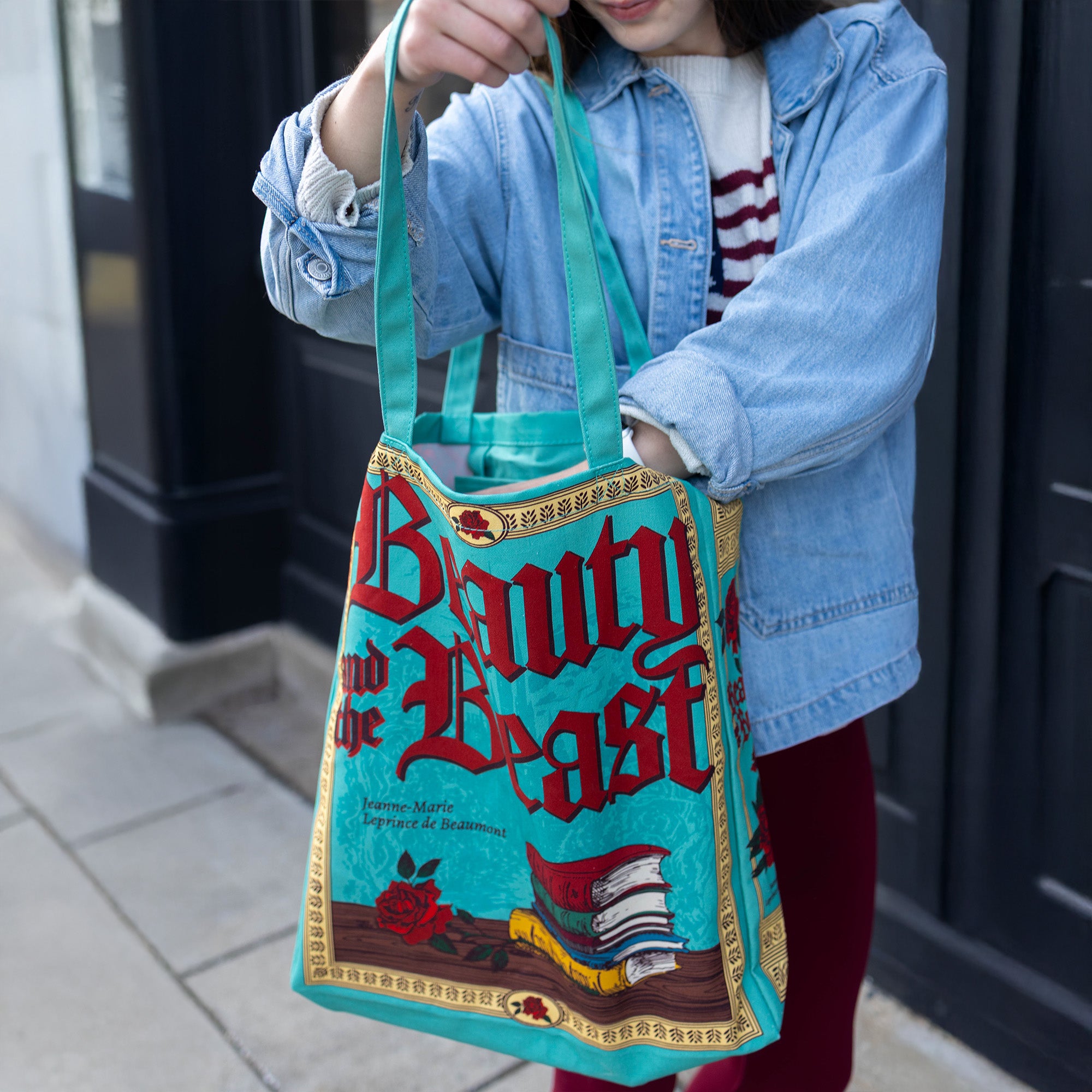 Person holding a 'Beauty and the Beast' book-themed bag on a sidewalk.