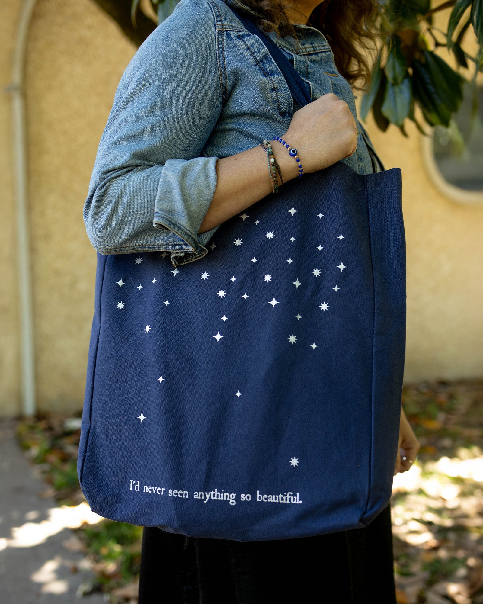 model carrying navy tote bag with star pattern and 'I'D NEVER SEEN ANYTHING SO BEAUTIFUL'