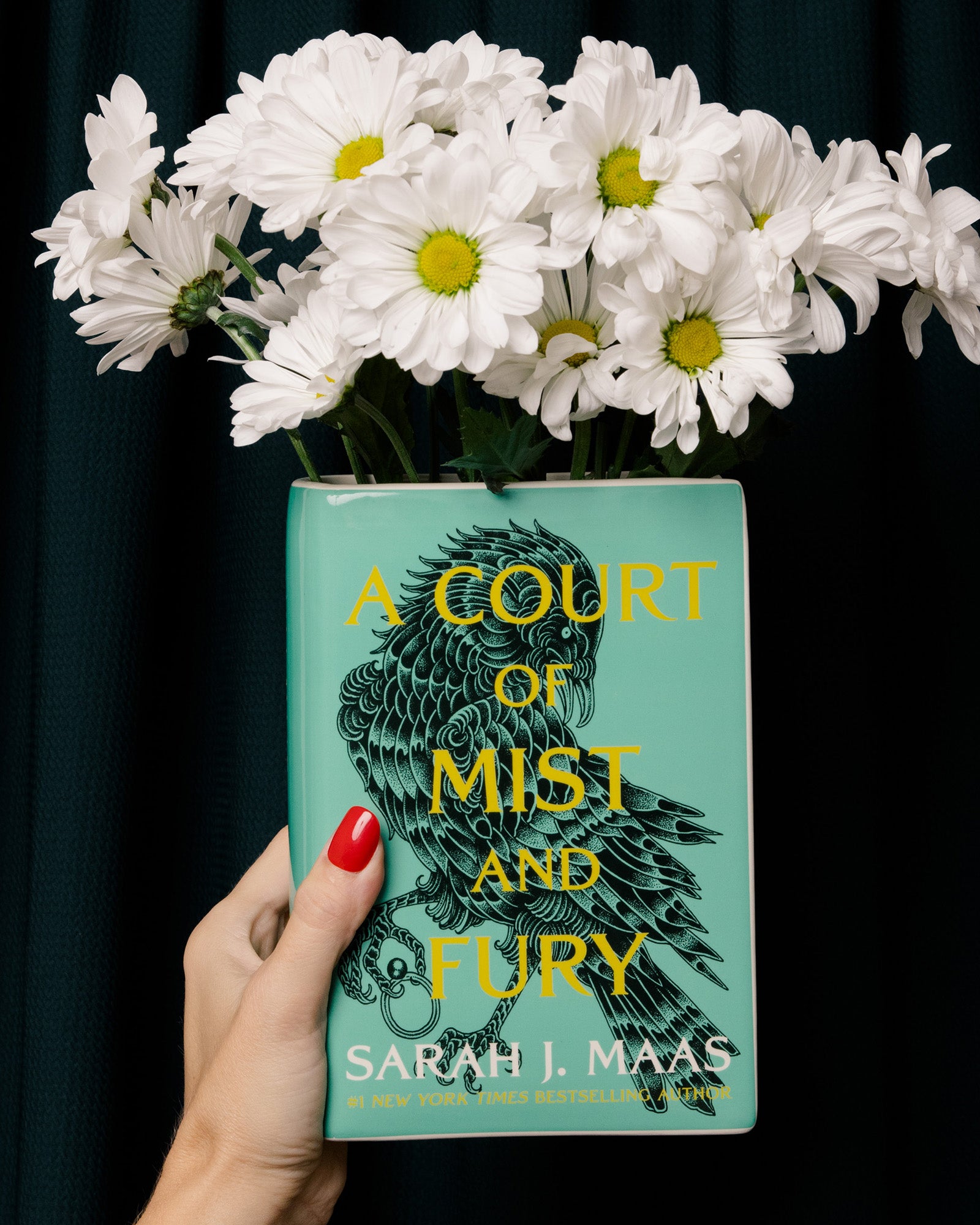 model holding 'A Court of Mist and Fury' by Sarah J. Maas vase with a green cover and white spine and white flowers inside
