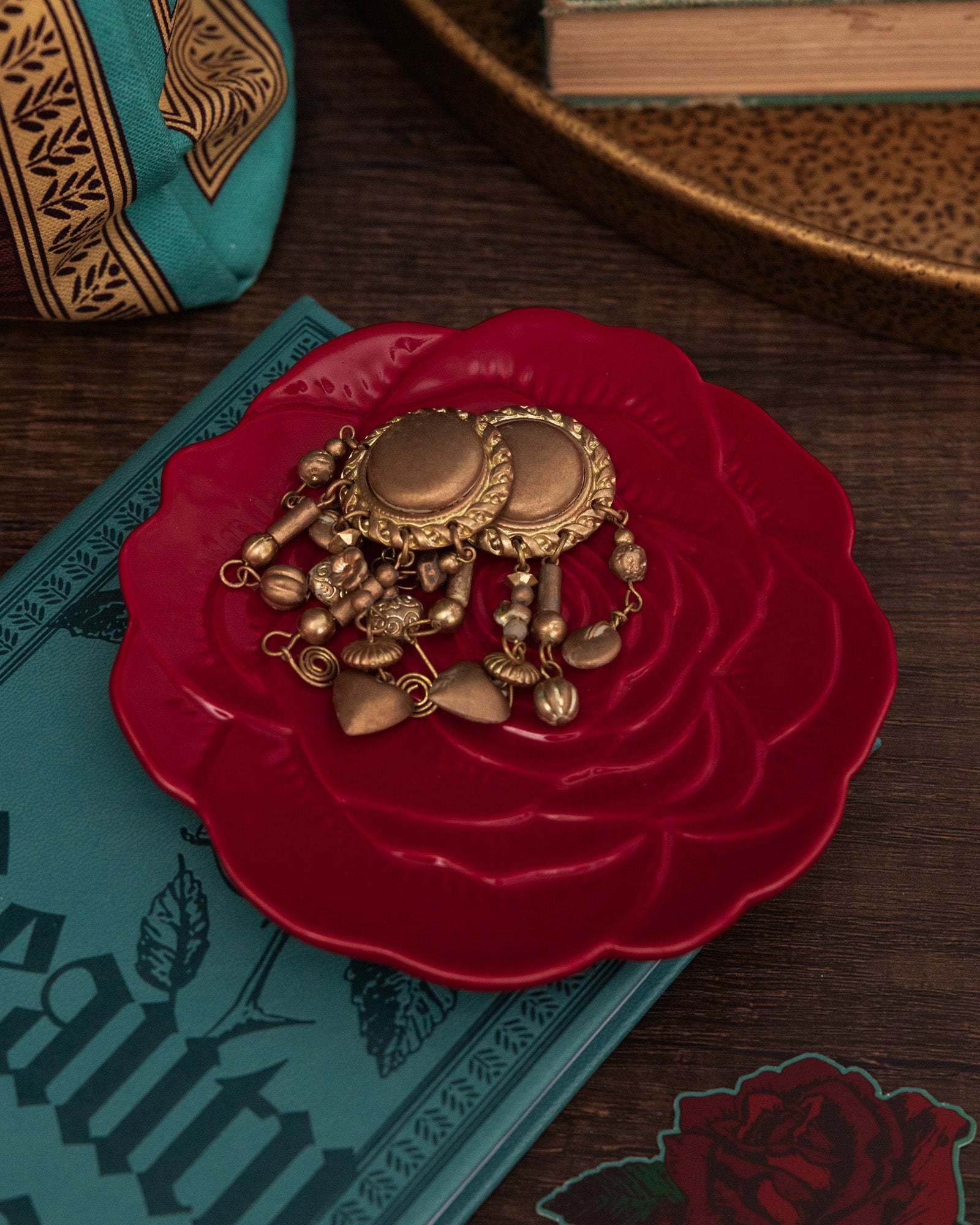 Gold jewelry on a red rose-shaped dish with a book and decorative items in the background