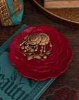 Gold jewelry on a red rose-shaped dish with a book and decorative items in the background