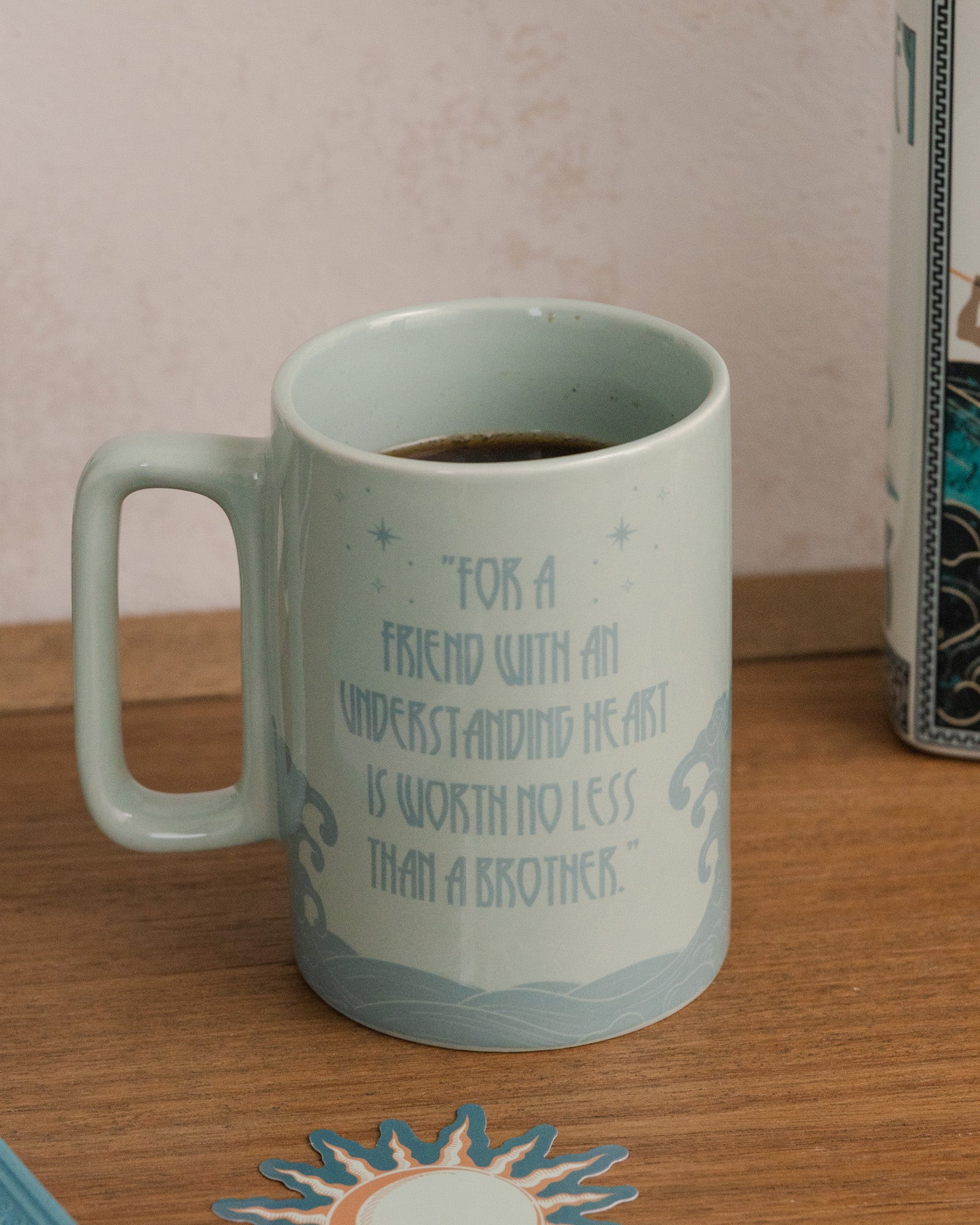 Teal mug with motivational quote on a wooden surface next to a box