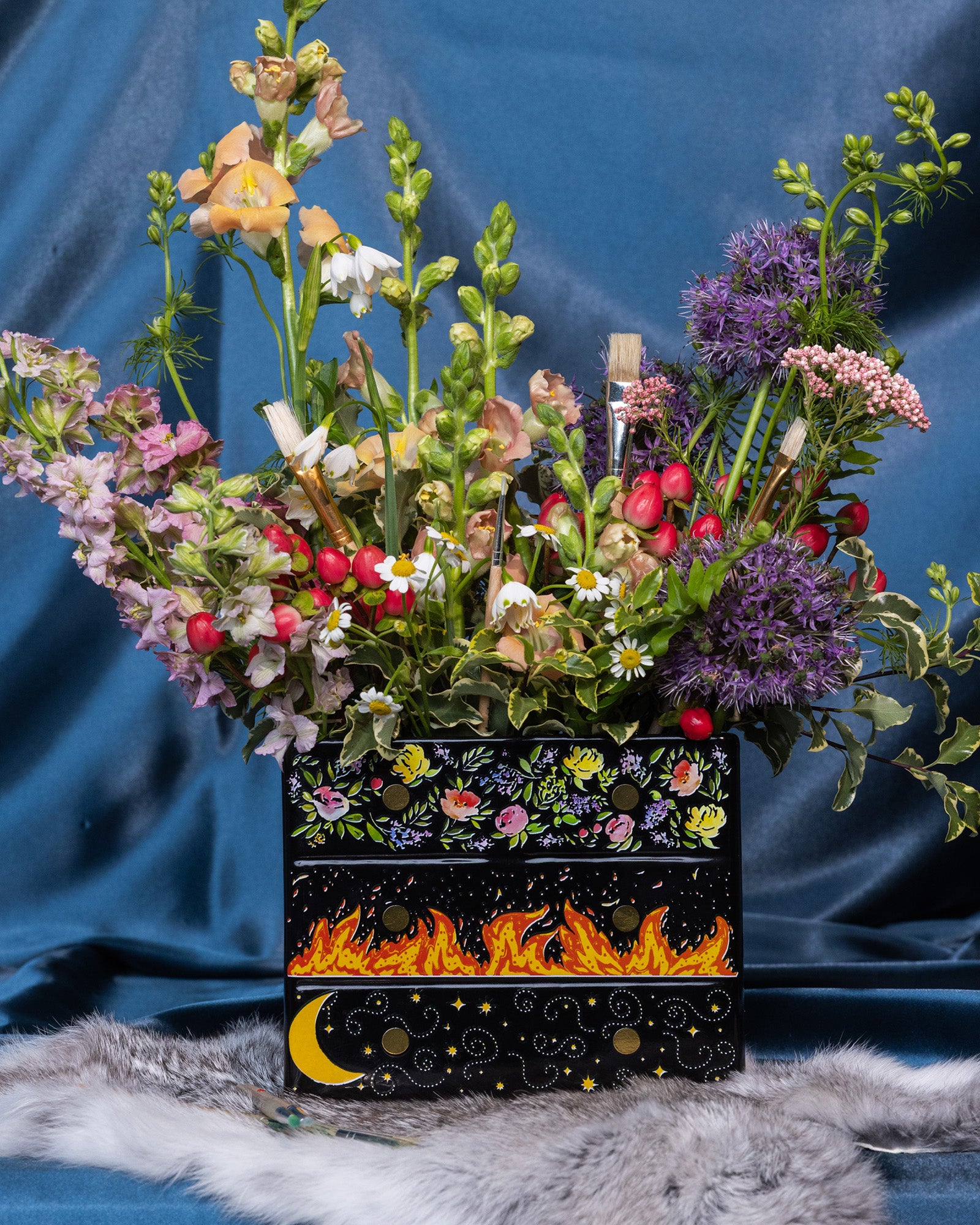 Black planter with floral and fiery designs with a bouquet inside