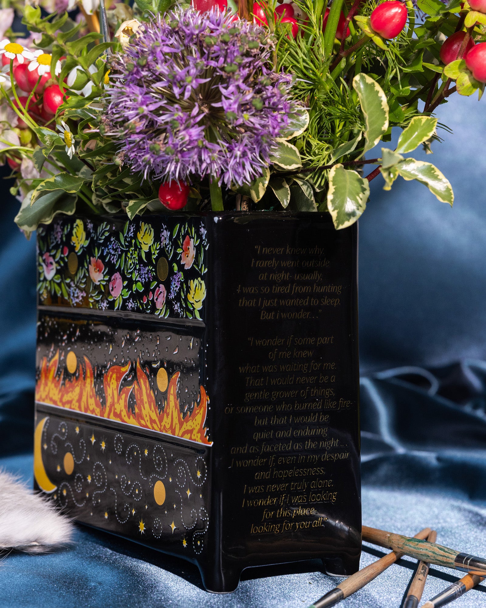 side view of Black planter with floral and fiery designs with a bouquet inside