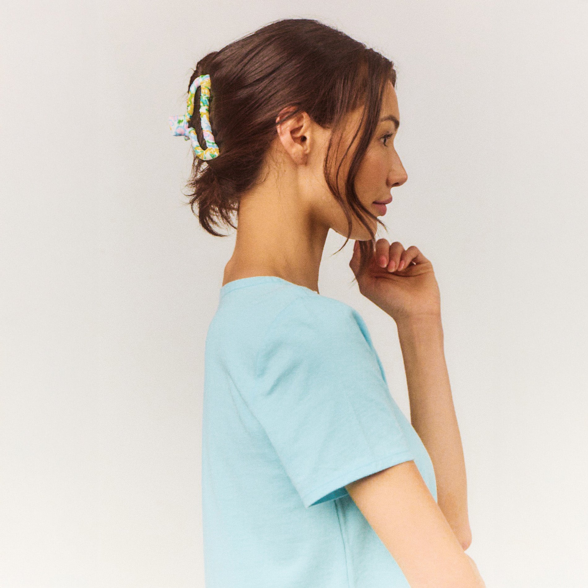 Woman wearing a light blue top against a plain background with a colorful hair claw