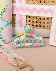 Floral-patterned strap with a gold clasp on a textured surface, with a wicker basket and floral fabric in the background.
