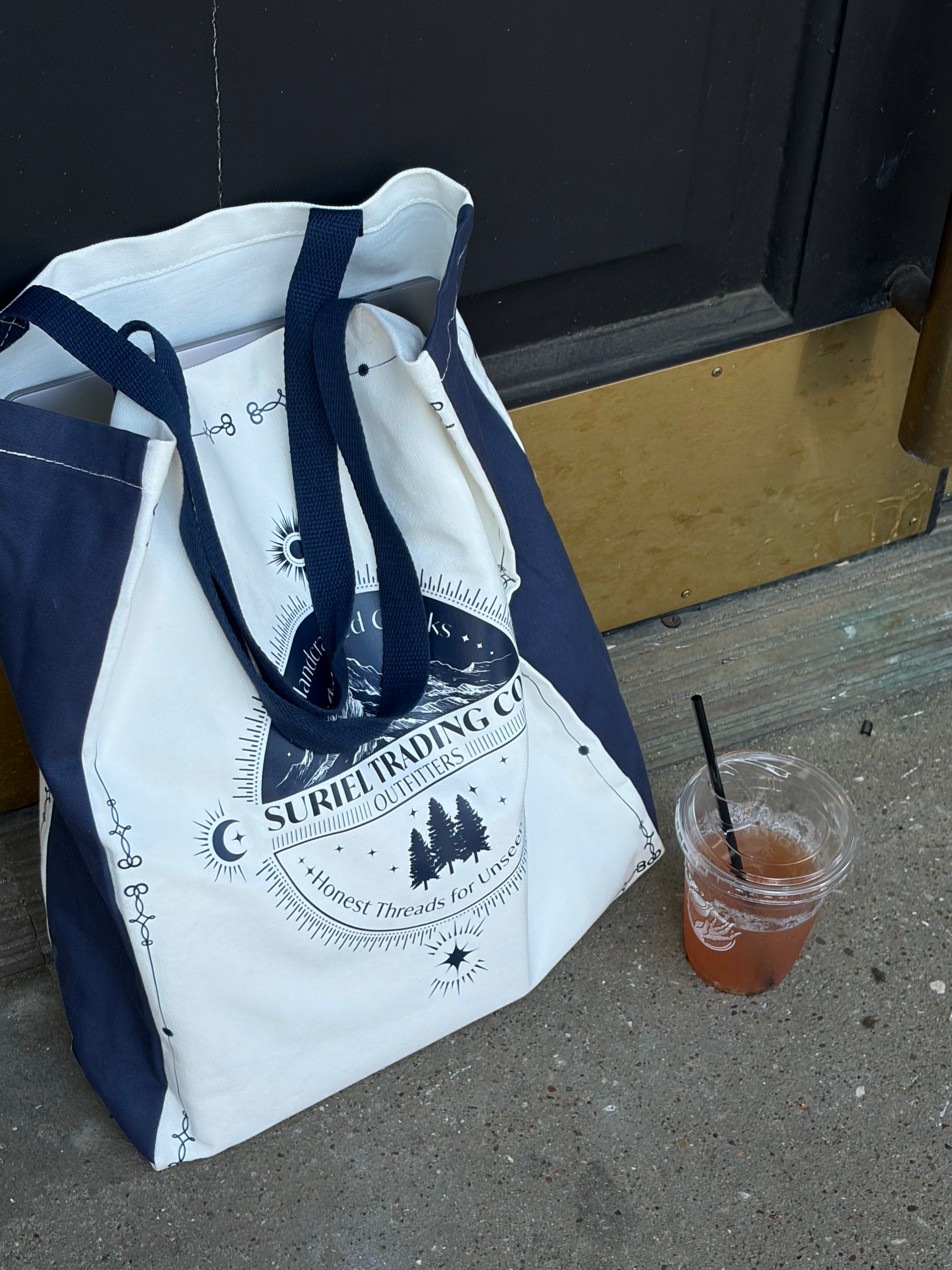 suriel trading co tote bag with a beverage next to it