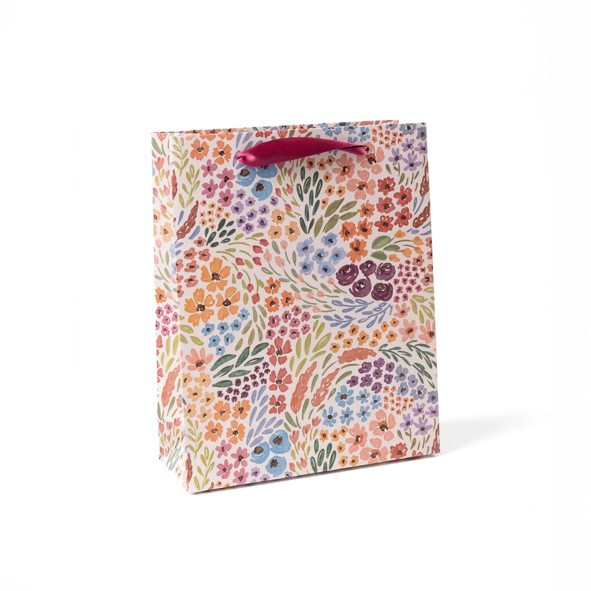 Colorful floral patterned gift bag with a pink handle on a white background