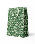 side view of green paper gift bag with white leaf pattern on a white background