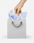 Model pulling white and lavender floral tissue paper out of white gift bag