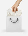 model pulling decorative tissue paper with gold floral pattern out of a silver gift bag