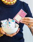 Person holding a bowl with playing cards and a deck of cards on a plain background