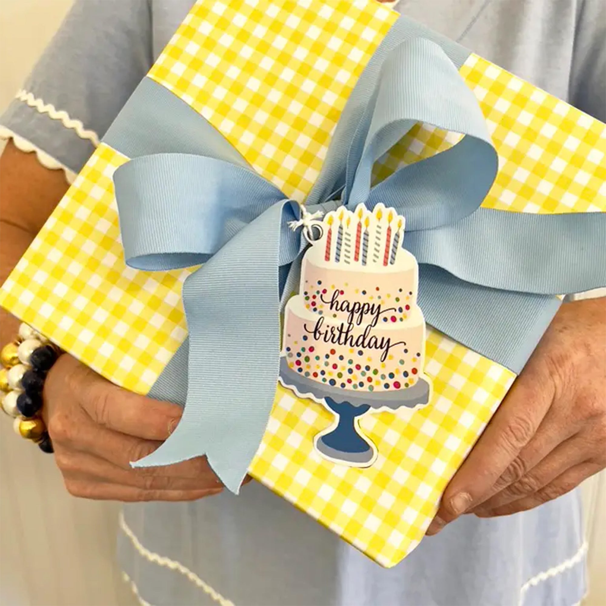 Gift wrapped in yellow checkered paper with a blue ribbon and 'Happy Birthday' cake tag.