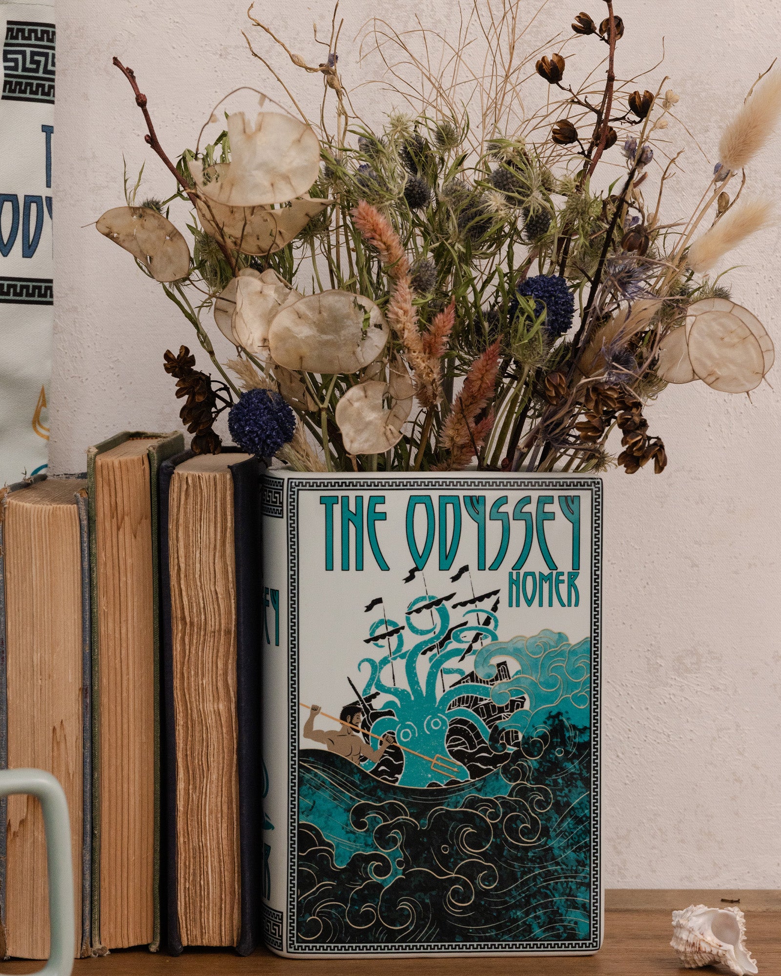 Book titled 'The Odyssey' by Homer with a decorative vase containing dried flowers on a wooden surface.