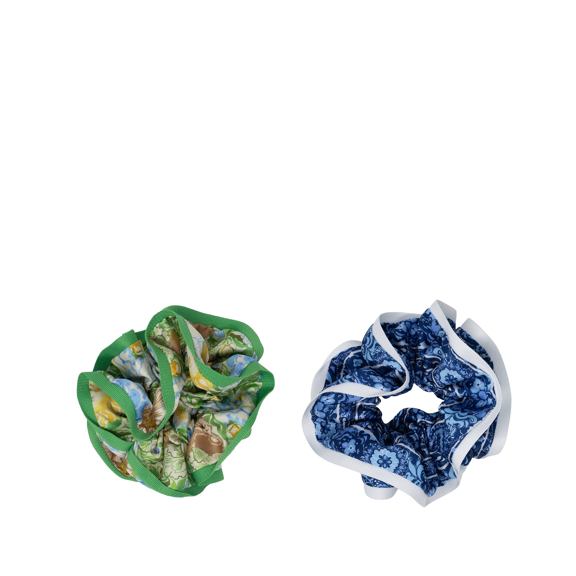 Two fabric scrunchies on a plain white background: one with a green border and a multicolor nature print, and one with a blue and white marbled pattern and white border.