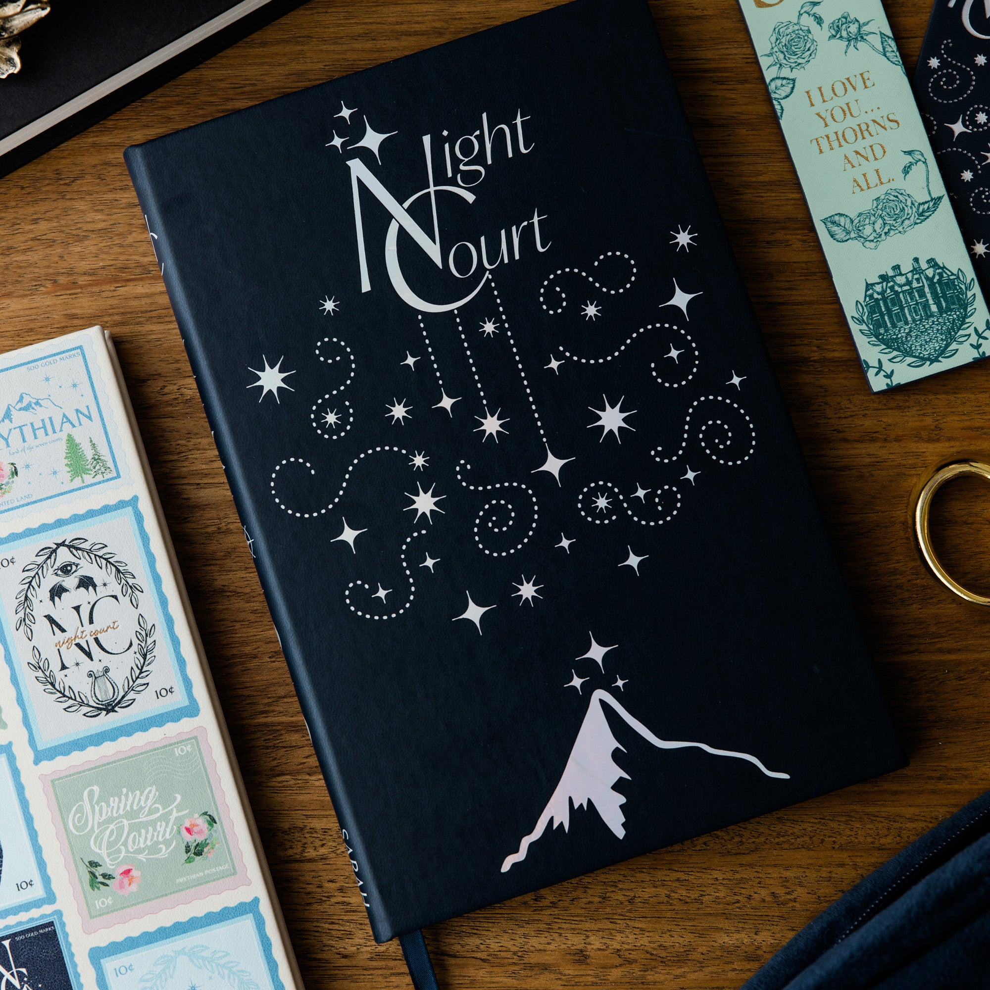 Black notebook with white star design and 'Night Court' text on a wooden surface